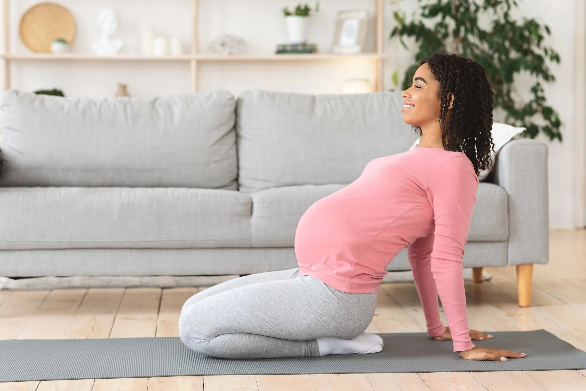 Hochschwangere Frau bei einer sanften Dehnübung auf der Yogamatte im Wohnzimmer