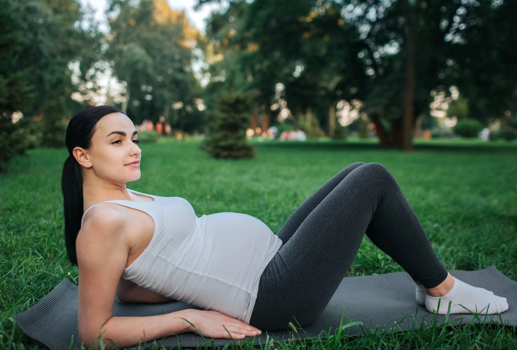 Schwangere Frau macht eine Pause auf der Trainingsmatte im Park und hört in sich hinein